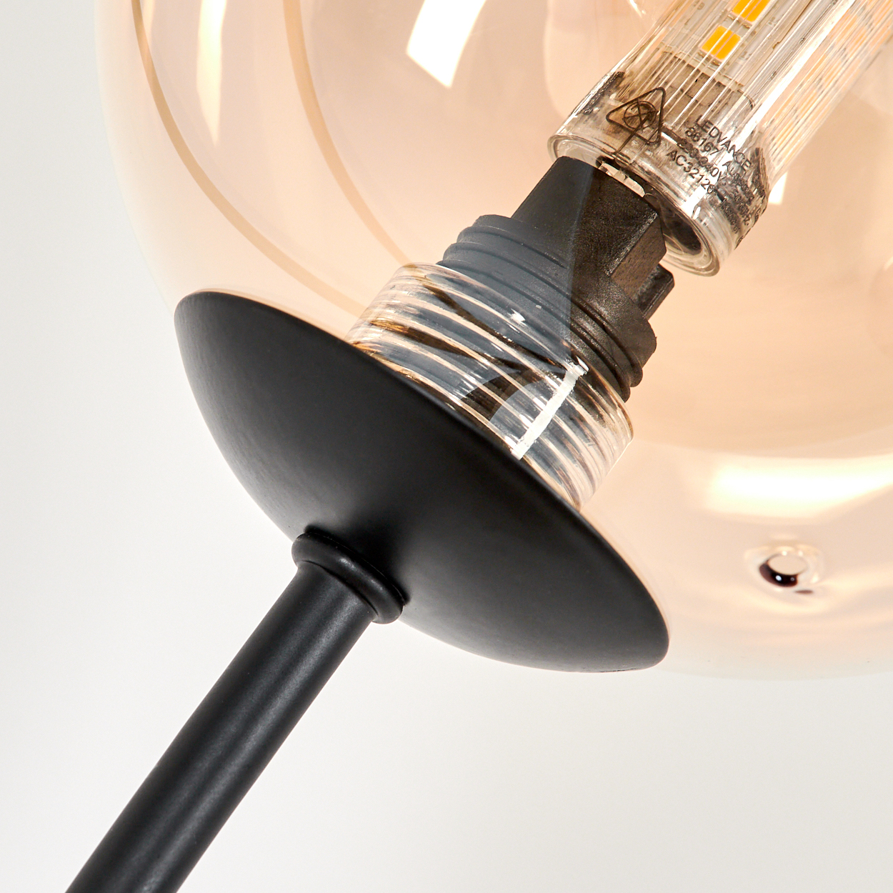 Nahaufnahme einer schwarzen Lampe mit bernsteinfarbenen Glaskugeln. Die Glühbirne ist sichtbar.