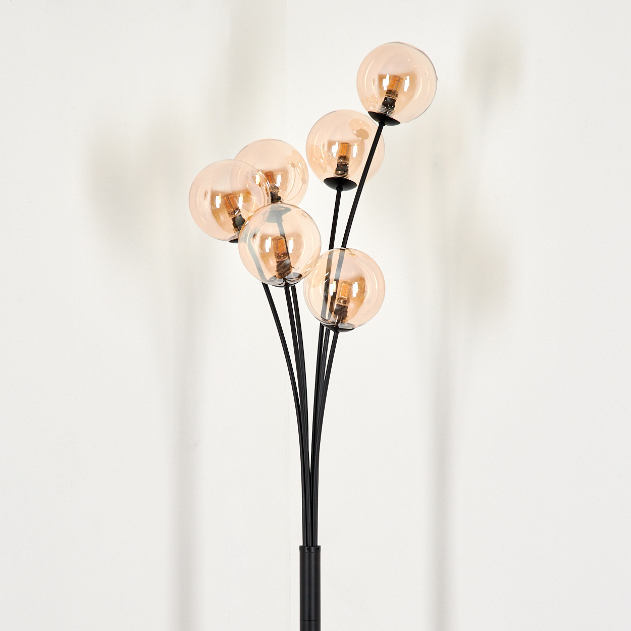 Eine schwarze Stehlampe mit bernsteinfarbenen Glaskugeln. Die Lampe steht auf weißem Grund.