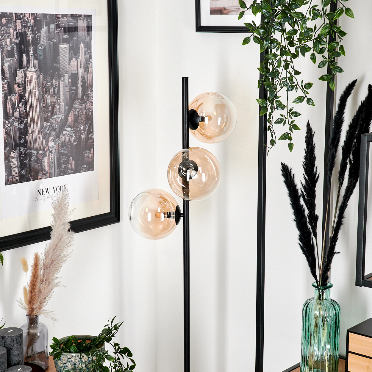 Eine schwarze Stehlampe mit drei bernsteinfarbenen Glaskugeln. Ein New York-Bild. Der Hintergrund ist eine Raumeinrichtung.