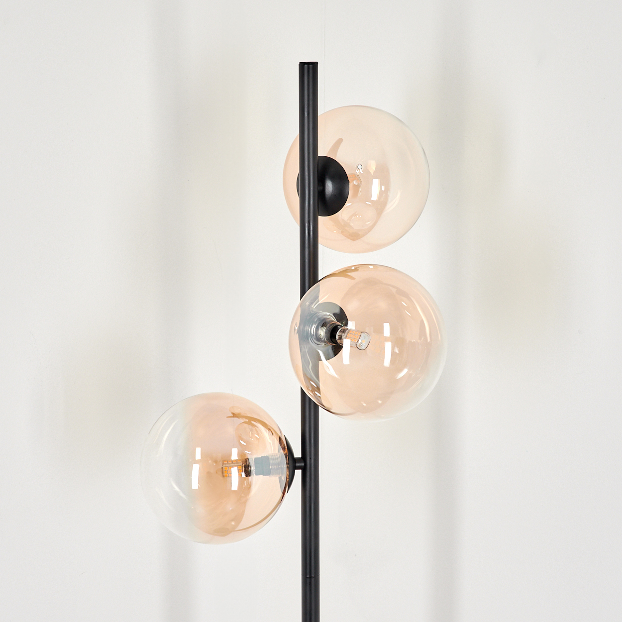 Eine schwarze Stehlampe mit drei bernsteinfarbenen Glaskugeln vor weißem Hintergrund.