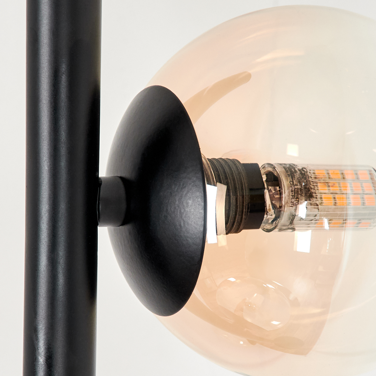 Nahaufnahme von bernsteinfarbener Kugel und schwarzem Stiel einer Lampe. Weißer Hintergrund.