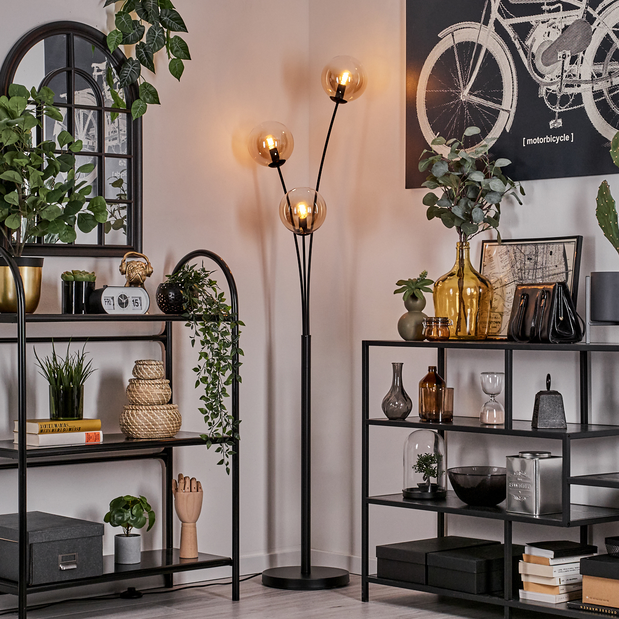 Zimmer mit schwarzen Regalen, Pflanzen und einer schwarzen Stehlampe mit bernsteinfarbenen Kugeln.