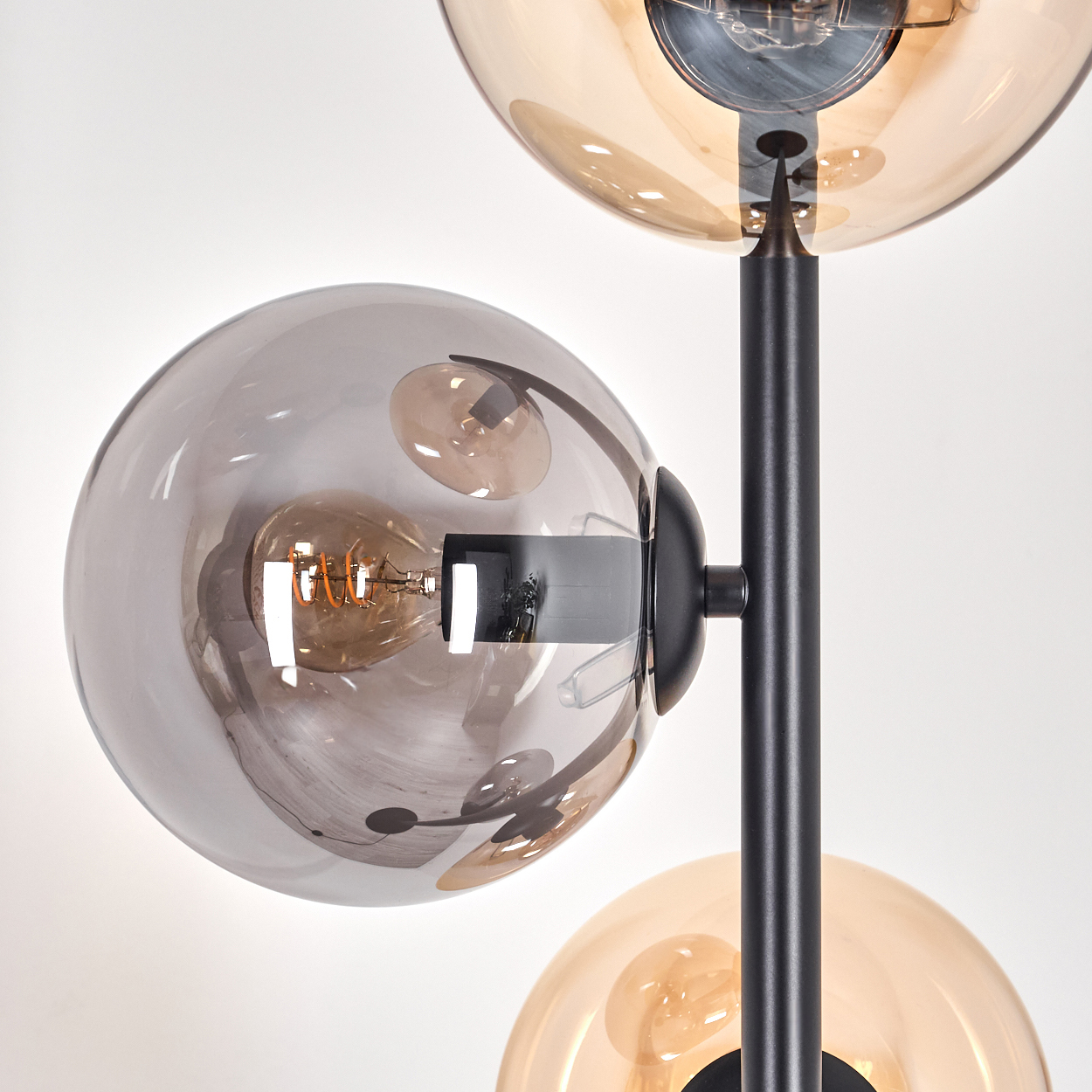 Nahaufnahme einer Lampe mit drei Glaskugeln. Die Details der Glühbirne und der schwarzen Struktur werden gezeigt.