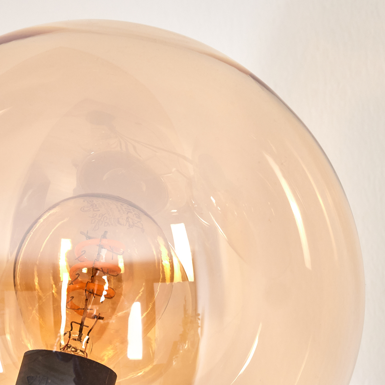 Nahaufnahme einer Glaskugel-Glühbirne. Zeigt das bernsteinfarbene Glas und das interne Leuchtelement.
