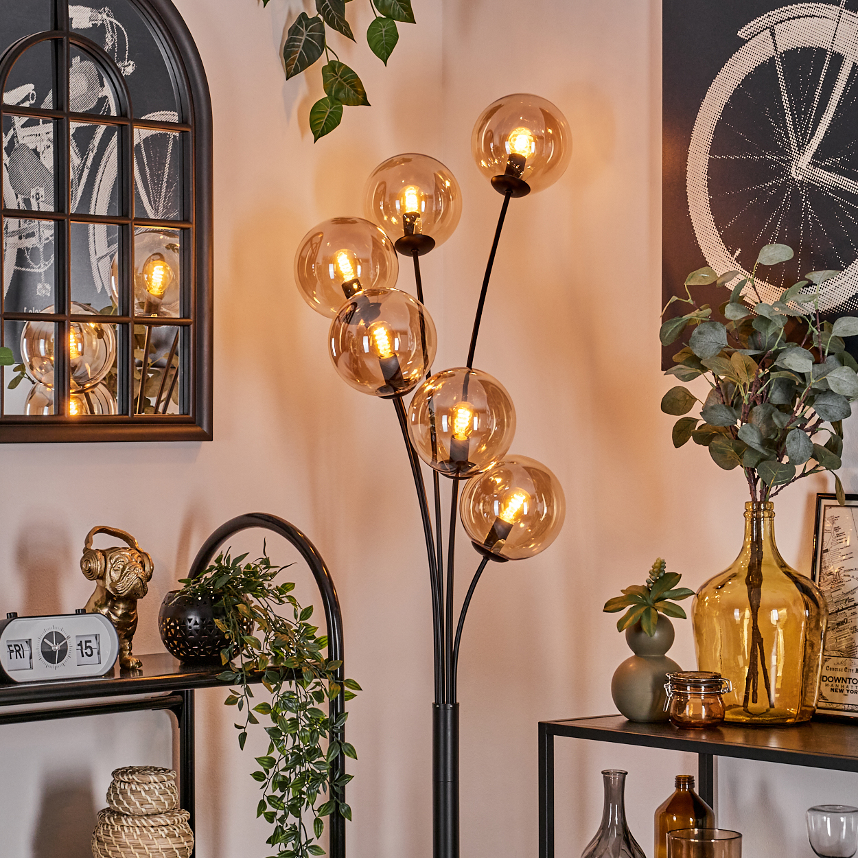 Stehlampe mit bernsteinfarbenen Glaskugelschirmen auf schwarzen Stielen. Die Lampe steht in einem Raum mit Dekoration.