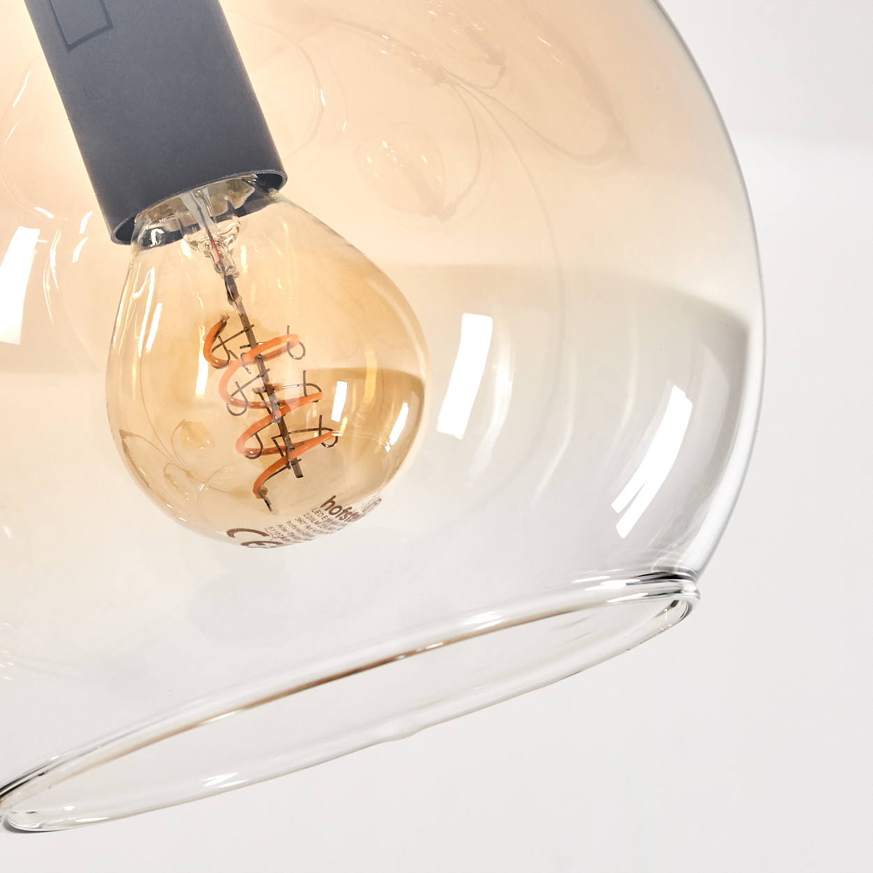 Nahaufnahme einer bernsteinfarbenen Glühbirne in einem Glaskugelschirm, mit Filament.