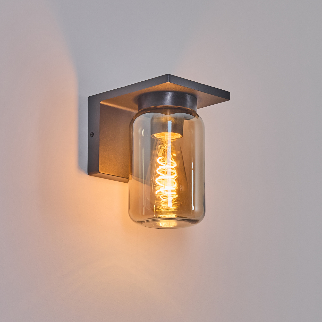 Schwarzes Wandlicht mit bernsteinfarbenem Gläser-Schirm, beleuchtet, an der Wand.