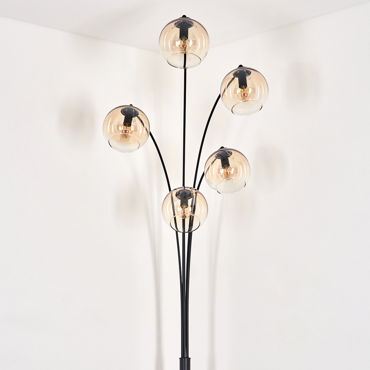 Schwarze Stehlampe mit fünf bernsteinfarbenen Glaskugeln in einer weißen Ecke.