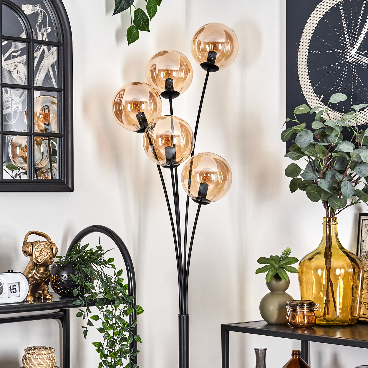 Stehlampe mit bernsteinfarbenen Glaskugeln, schwarzem Rahmen und Dekorationsartikeln in einem Raum.