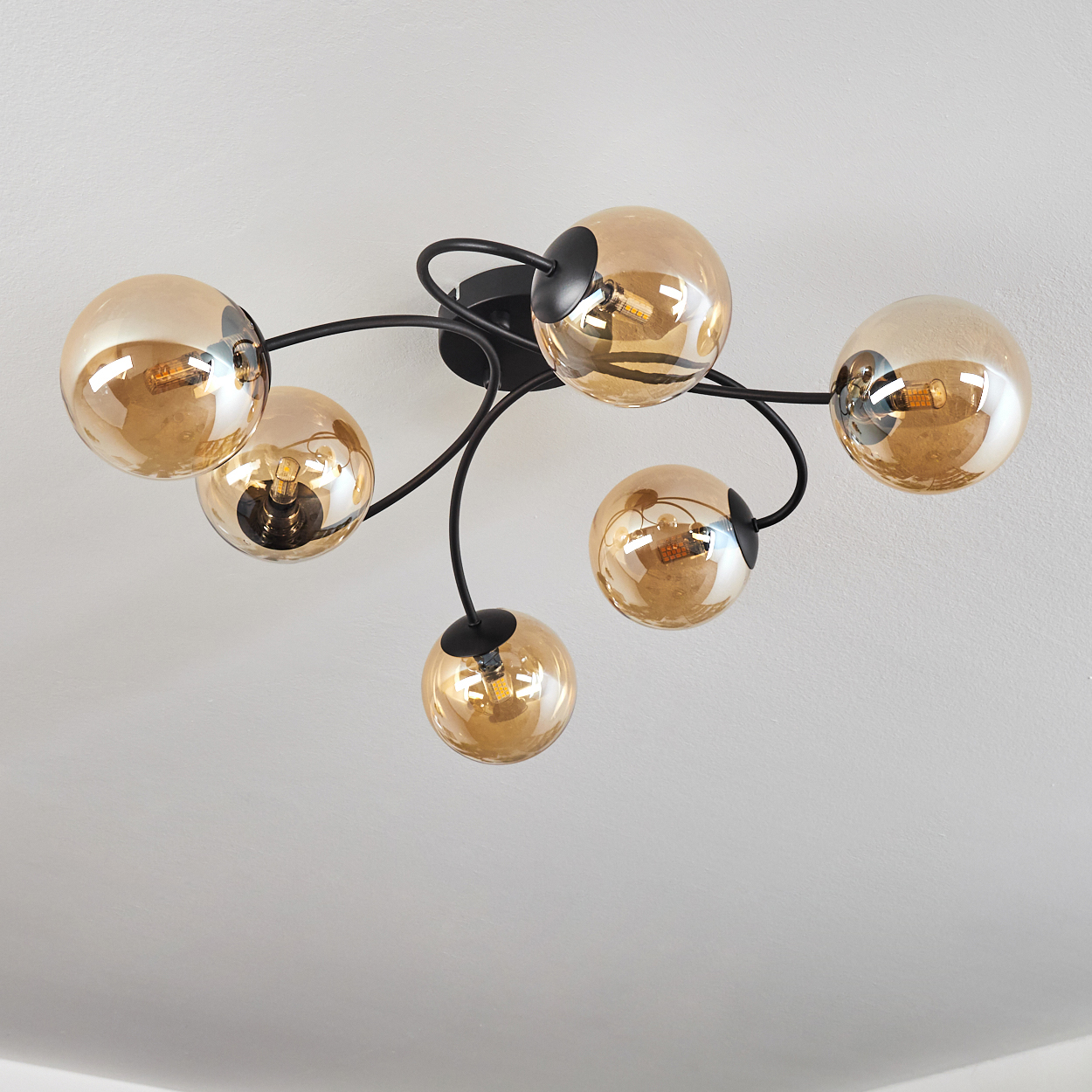 Deckenlampe mit sechs bernsteinfarbenen Glaskugeln an schwarzen, gebogenen Armen an weißer Decke.