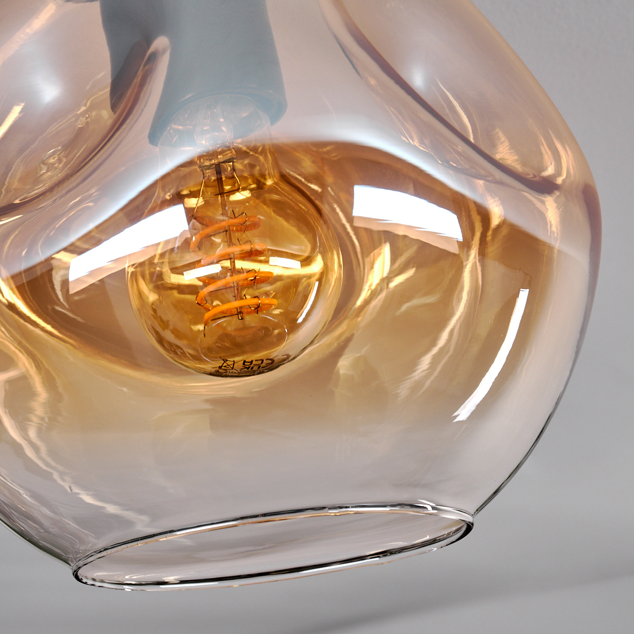 Nahaufnahme einer Glühbirne in einem goldfarbenen, bauchigen Glas. Das Glas hat eine einzigartige Form.