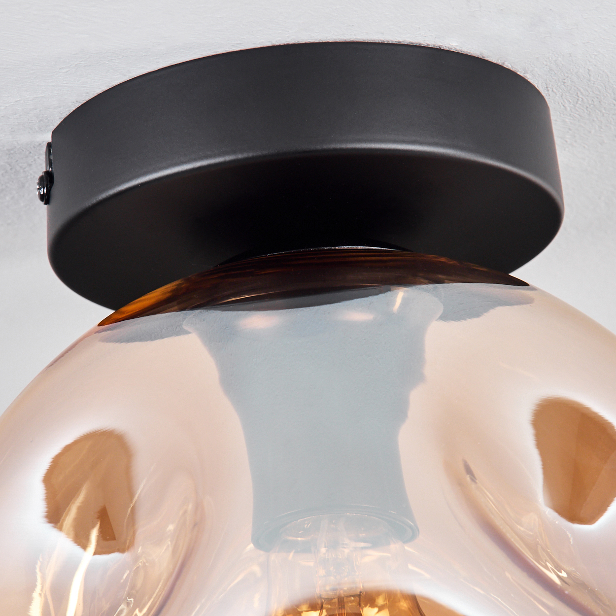 Nahaufnahme einer Deckenleuchte. Goldene Glaskugel und schwarze Basis. Das Licht ist eingeschaltet.