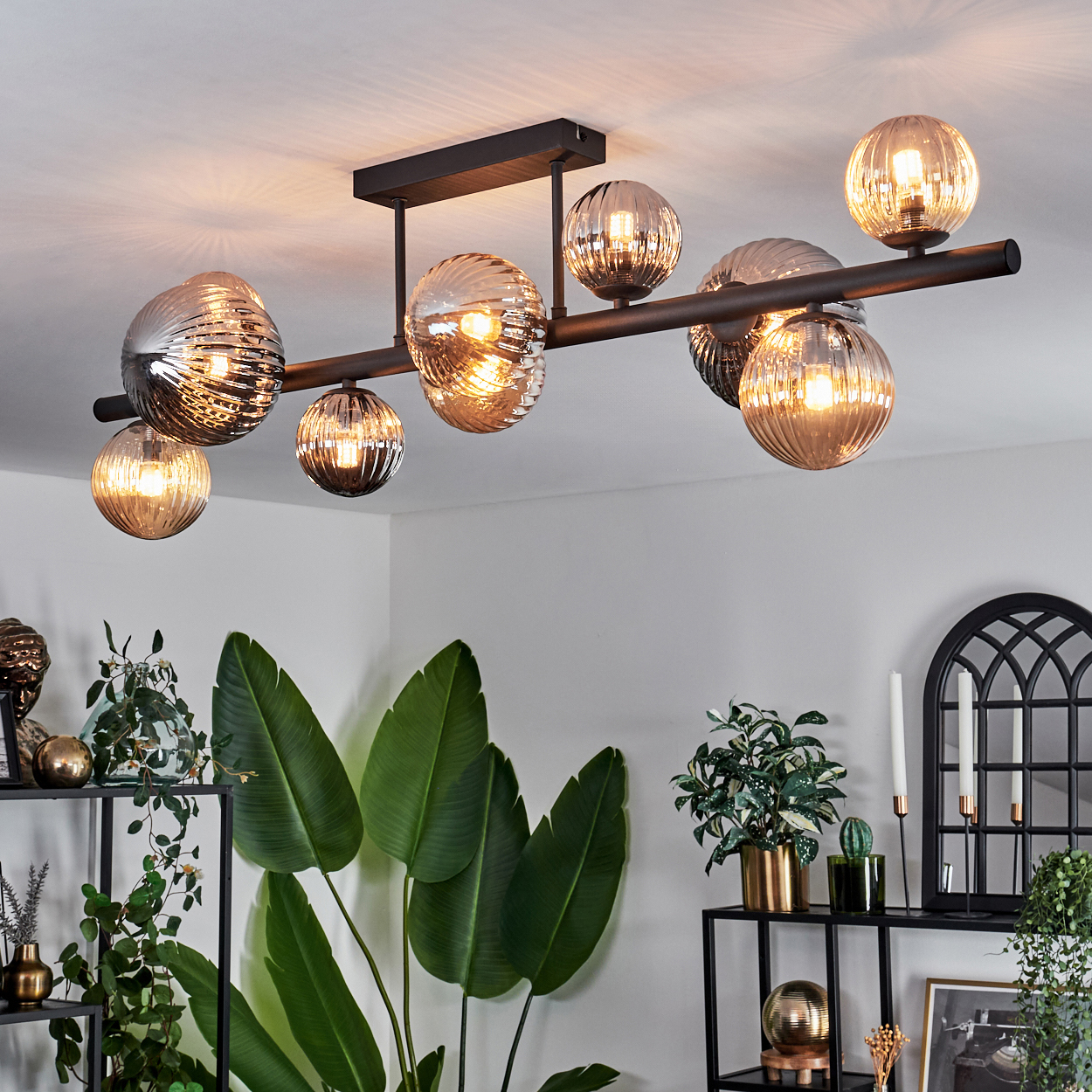 Deckenlampe mit mehreren Glaskugeln und schwarzen Balken, dargestellt in einem Wohnzimmer.