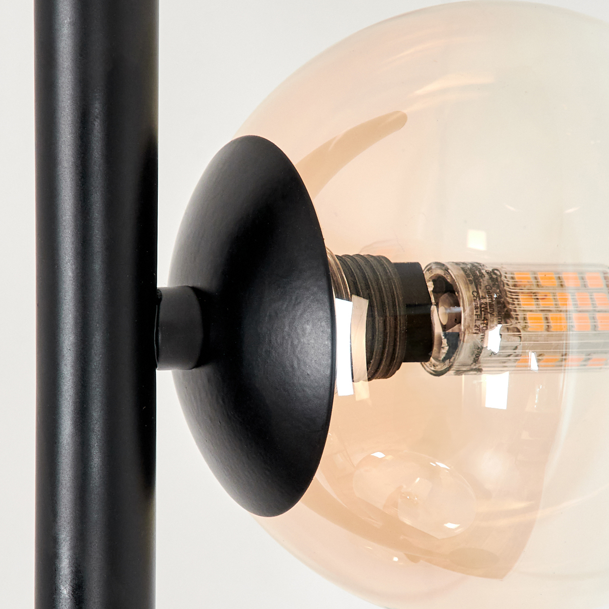 Nahaufnahme einer Lampe mit schwarzer Halterung und einer bernsteinfarbenen Glühbirne. Der Hintergrund ist weiß.
