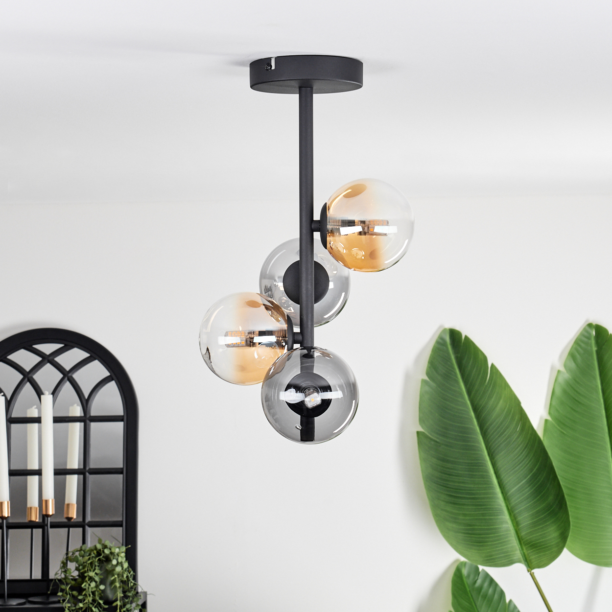 Deckenlampe mit drei Glaskugeln, bernsteinfarben und klar. Laubwerk und ein Fenster im Hintergrund.