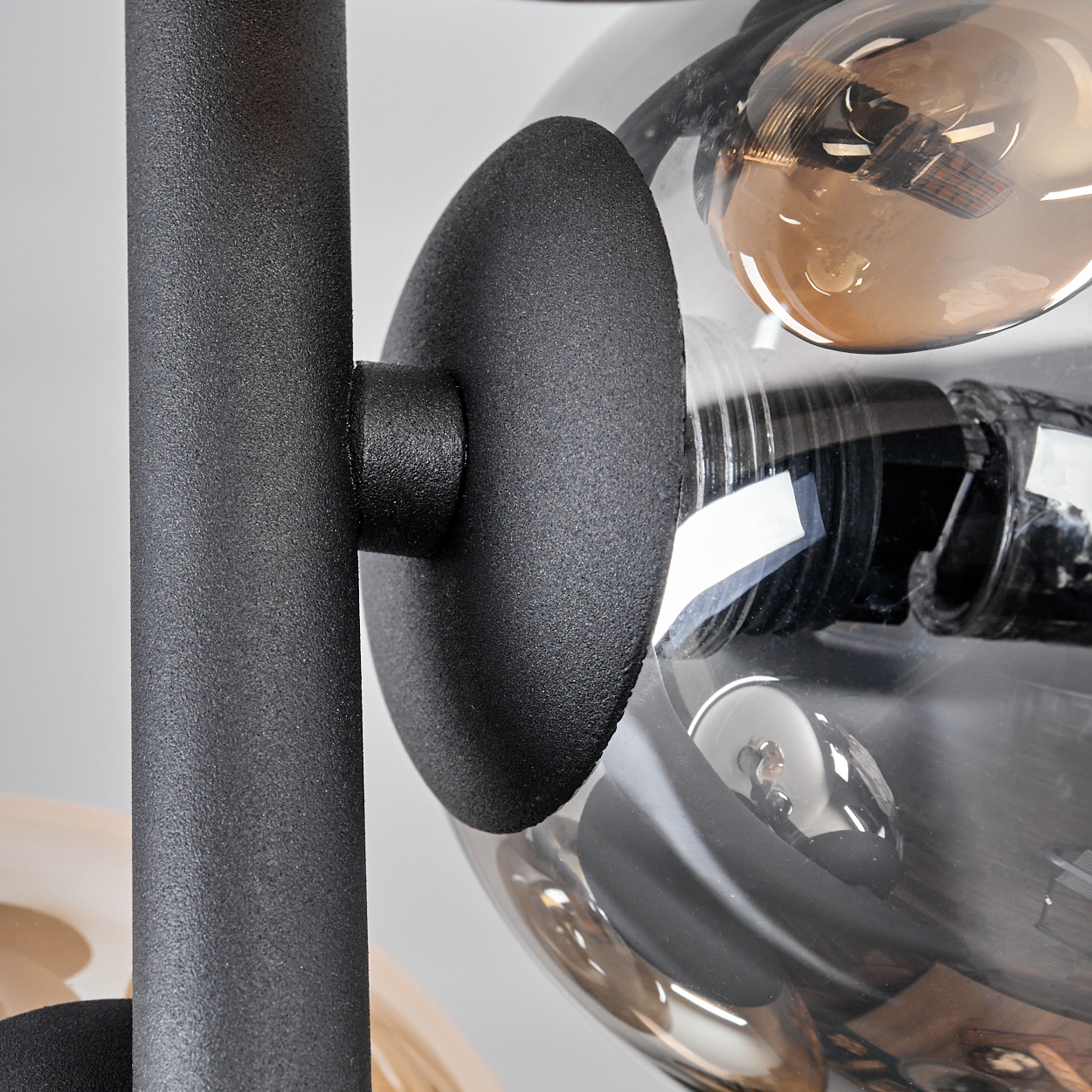 Nahaufnahme der Lampe mit schwarzer Halterung und bernsteinfarbenen und klaren Glaskolben. Weißer Hintergrund.