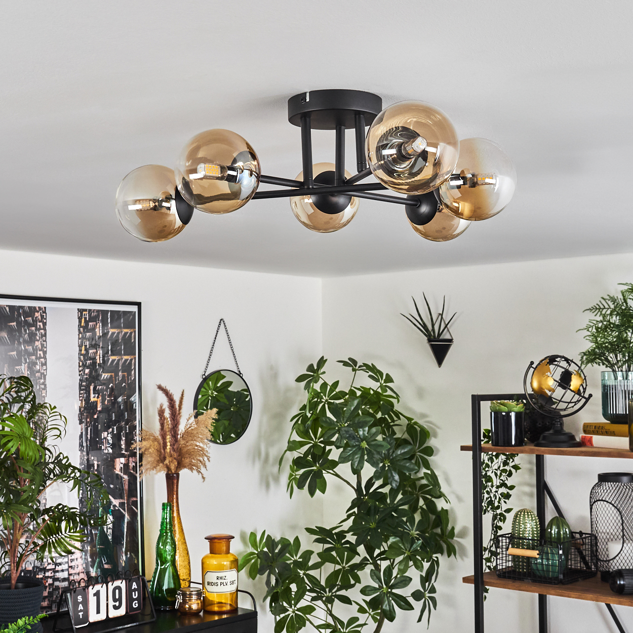 Deckenlampe mit sechs bernsteinfarbenen Kugeln, schwarzer Rahmen. Pflanzen, Spiegel und Deko im Hintergrund.