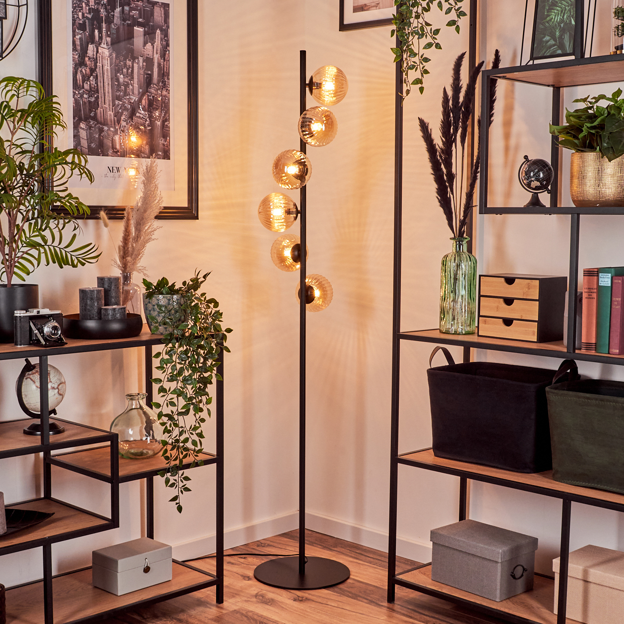 Interieur mit Stehlampe, schwarzen Regalen, Pflanzen und Kunstwerken mit New York-Thema.