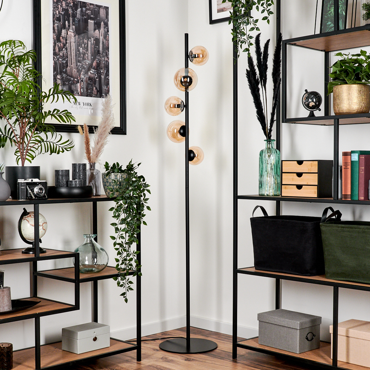 Schwarze Stehlampe mit bernsteinfarbenen Glühbirnen. Ecke eines Zimmers mit Regalen, Dekoration und einem New York Bild.