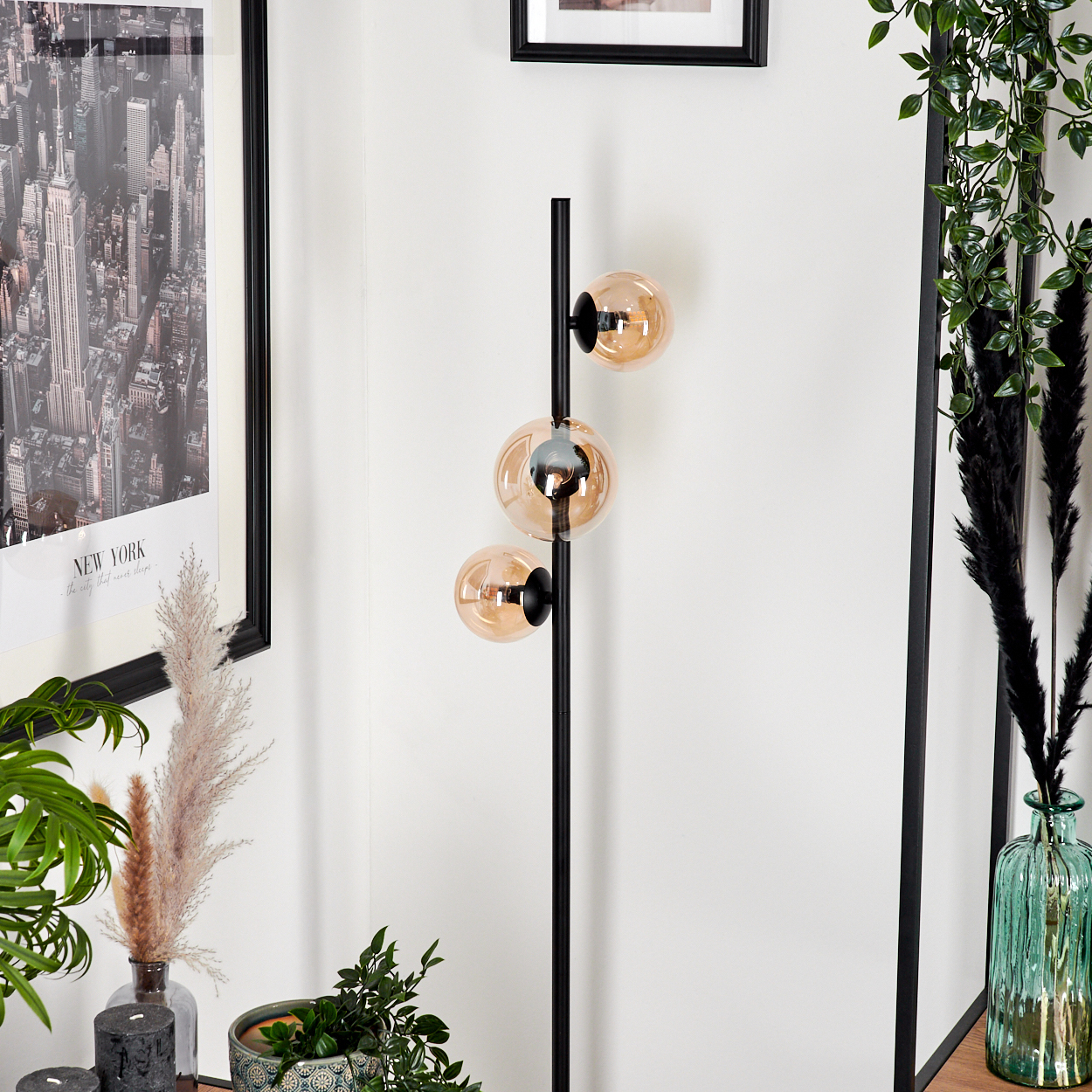 Schwarze Stehlampe mit drei bernsteinfarbenen Kugeln. Hintergrund: Wand, New York-Druck, Pflanzen und Dekor.