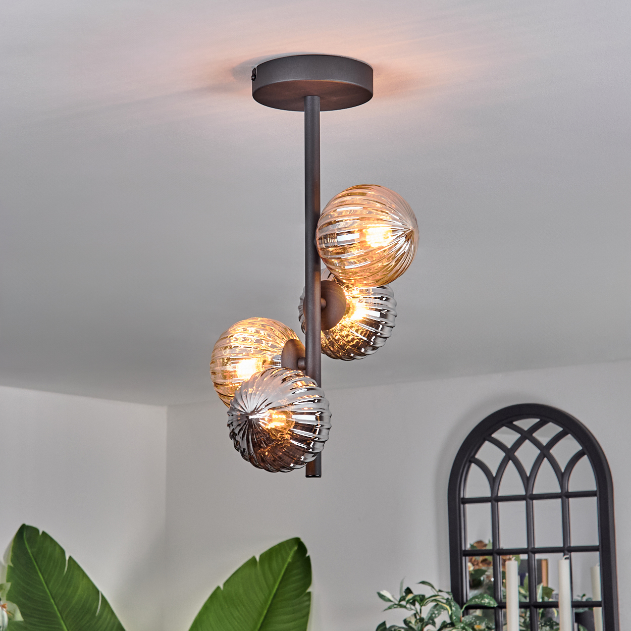 Deckenlampe mit vier gerippten Glaskugeln in Bernstein und Silber, die an einer schwarzen Stange hängen.