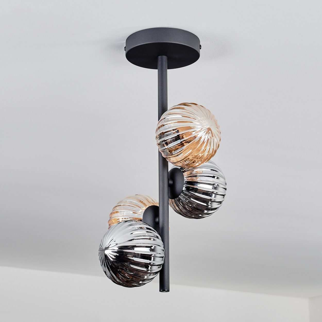 Deckenlampe mit vier gerippten Glaskugeln in Bernstein und Silber, die an einer schwarzen Stange hängen.