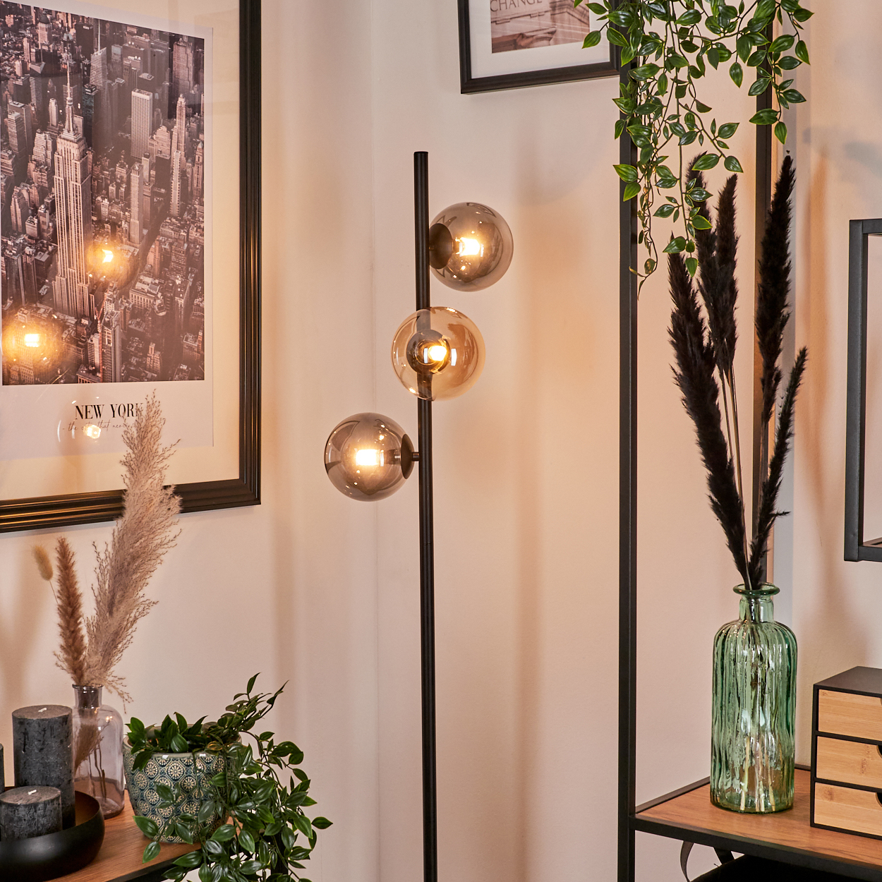 Eine Lampe mit drei bernsteinfarbenen Glaskugeln und Dekorationen in einem Innenraum. Ein New York-Druck hängt an der Wand.