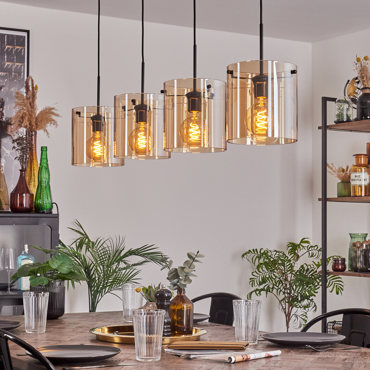 Ein Esszimmer mit einem Tisch und vier Lampen mit bernsteinfarbenen Glasschirmen. Pflanzen und Gläser auf dem Tisch.