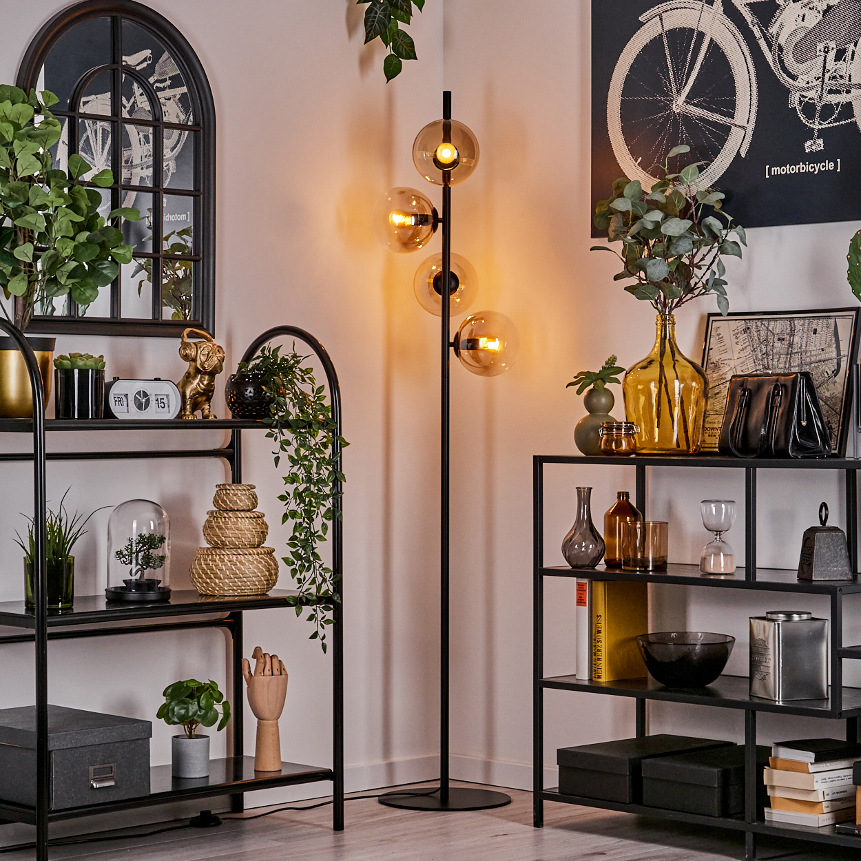 Interieur mit einer Stehlampe mit 4 bernsteinfarbenen Kugeln. Enthält Regale, Pflanzen und dekorative Objekte.