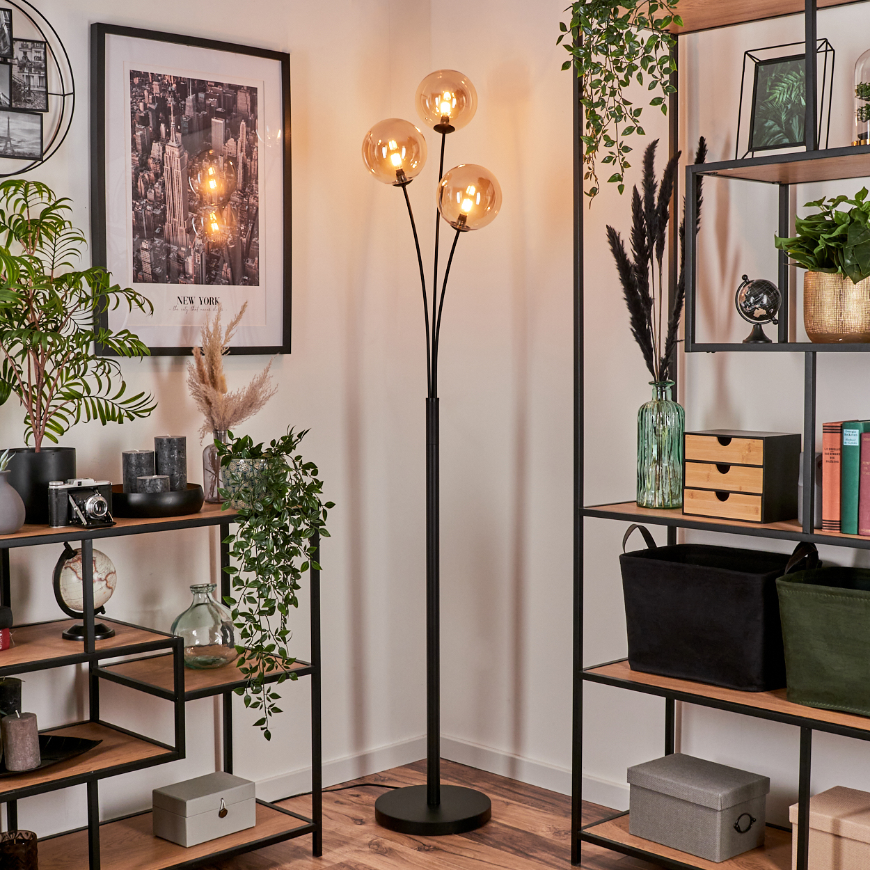 Eckszene mit schwarzer Stehlampe mit bernsteinfarbenen Glaskugeln, Regalen, Pflanzen und New York-Bild an der Wand.