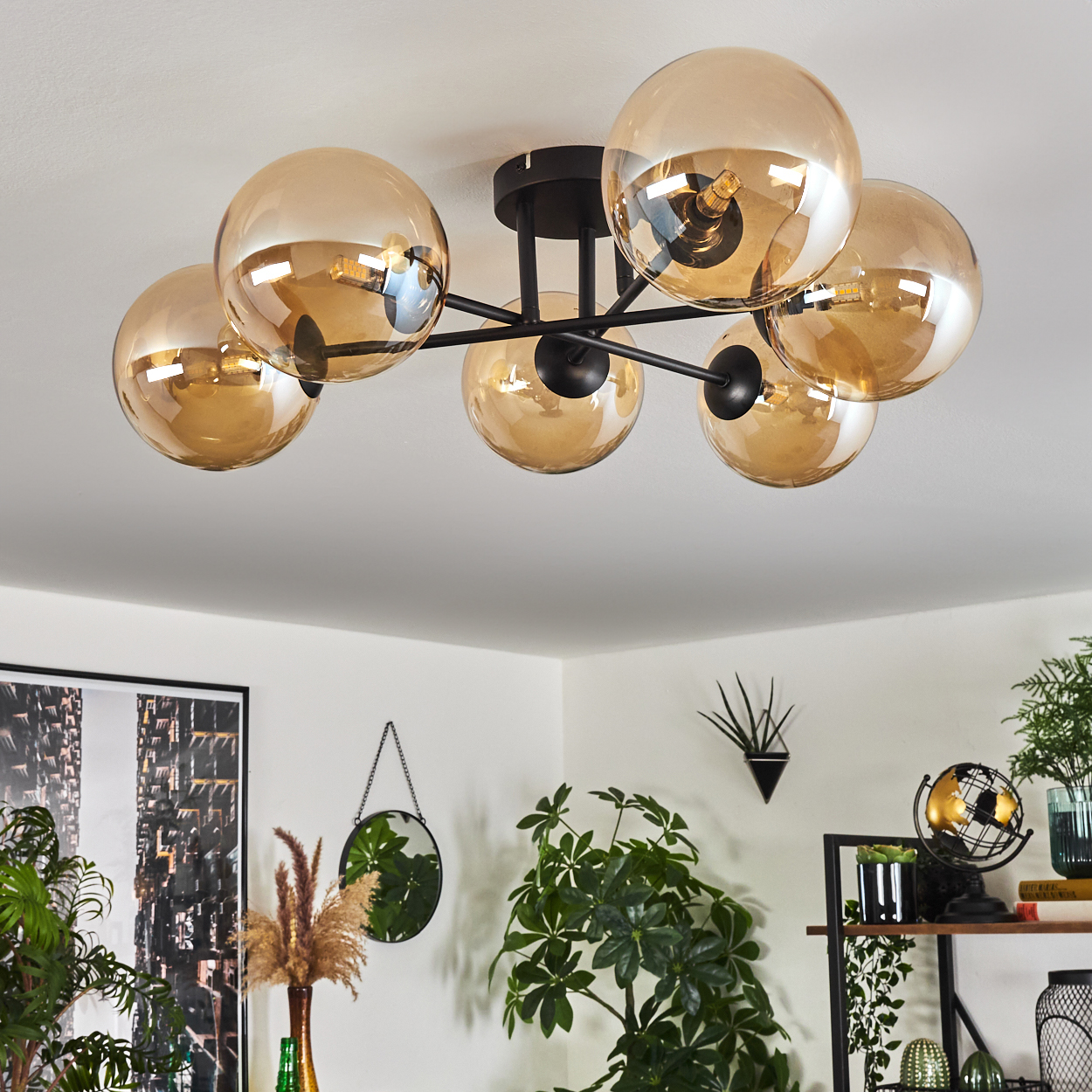 Deckenlampe mit sechs bernsteinfarbenen Glaskugeln an schwarzen Armen. Innenszene mit Pflanzen und Dekorationen.