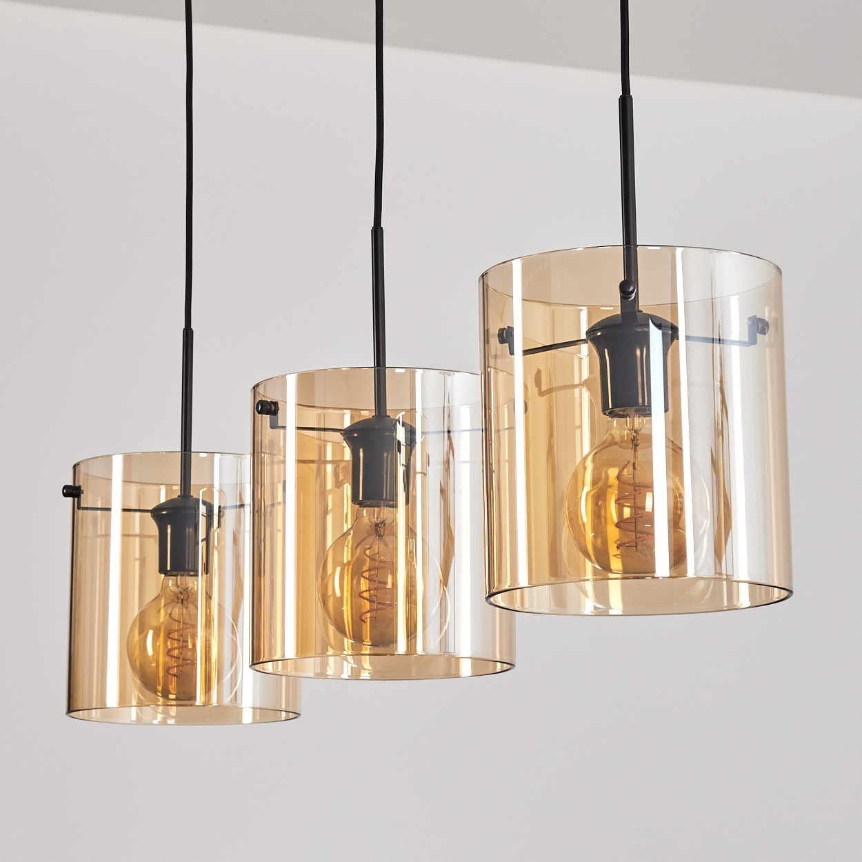 Drei Pendelleuchten mit zylindrischen, bernsteinfarbenen Glasschirmen. Weißer Hintergrund.