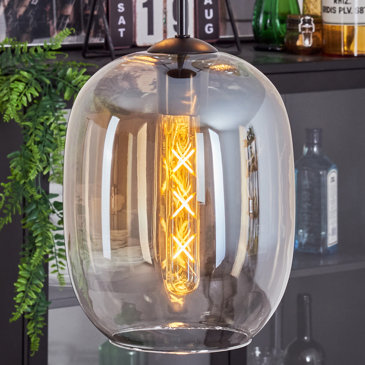 Nahaufnahme einer Pendelleuchte mit einem länglichen, bernsteinfarbenen Glasschirm, der mit warmem Licht leuchtet.