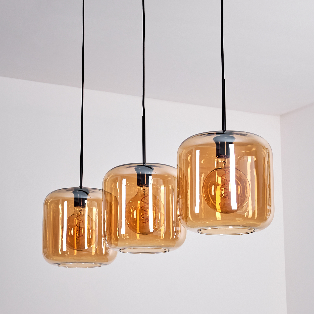 Drei bernsteinfarbene Glas-Pendelleuchten mit Edison-Glühbirnen, vor weißem Hintergrund.