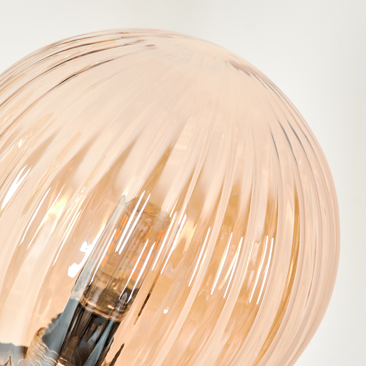 Nahaufnahme einer gerippten bernsteinfarbenen Glaskugellampe, die die Edison-Glühbirne zeigt.