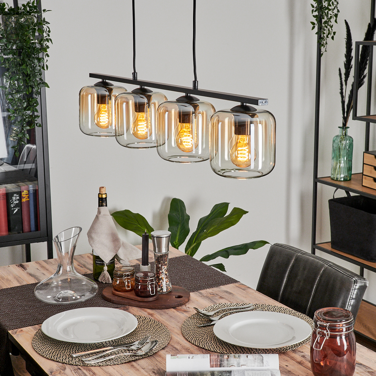 Esstisch mit Hängelampe. Die Lampe hat fünf Glasschirme. Teller, Gläser und Dekorationen stehen auf dem Tisch.
