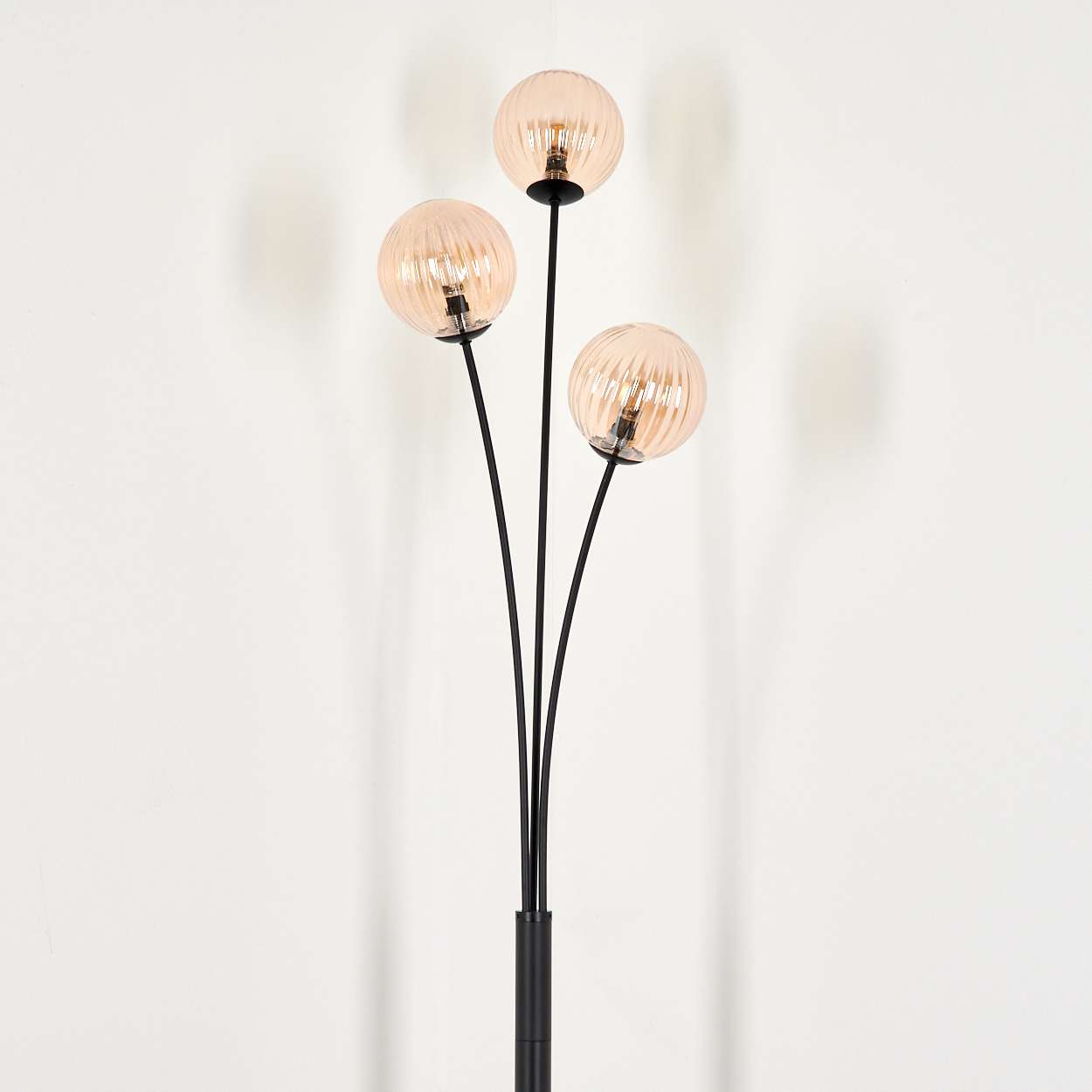 Eine Stehlampe mit drei bernsteinfarbenen Glaskugelschirmen auf weißem Hintergrund.