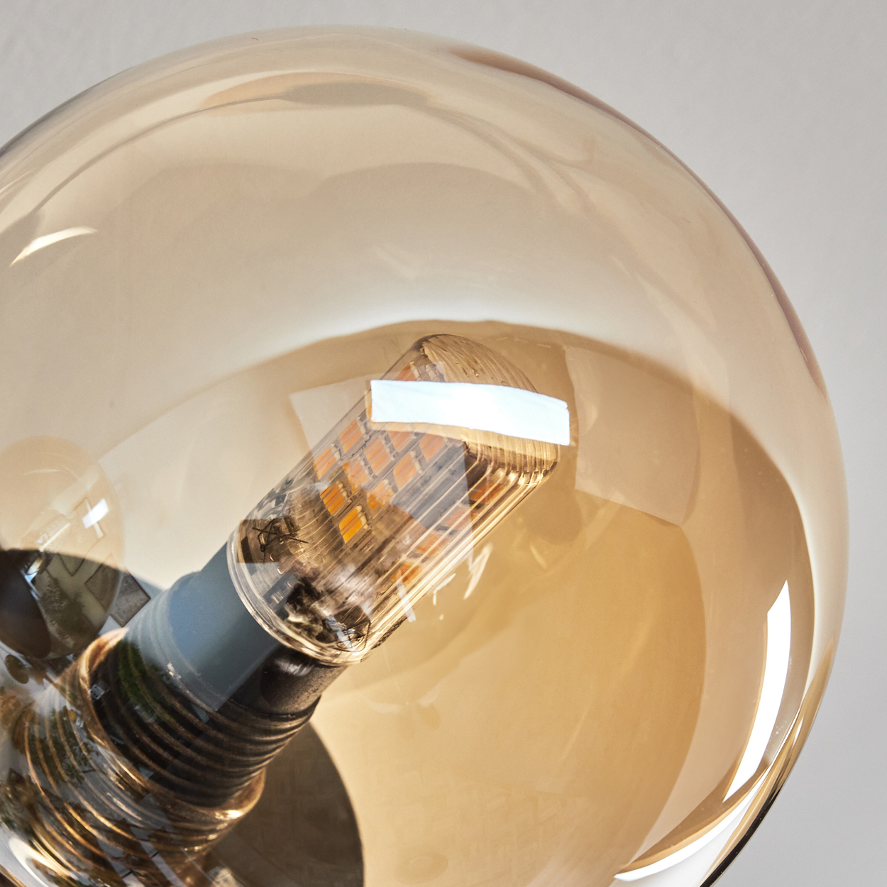Nahaufnahme einer Glühbirne in einer Glaskugel. Das Licht ist an. Die Glühbirne ist bernsteinfarben.