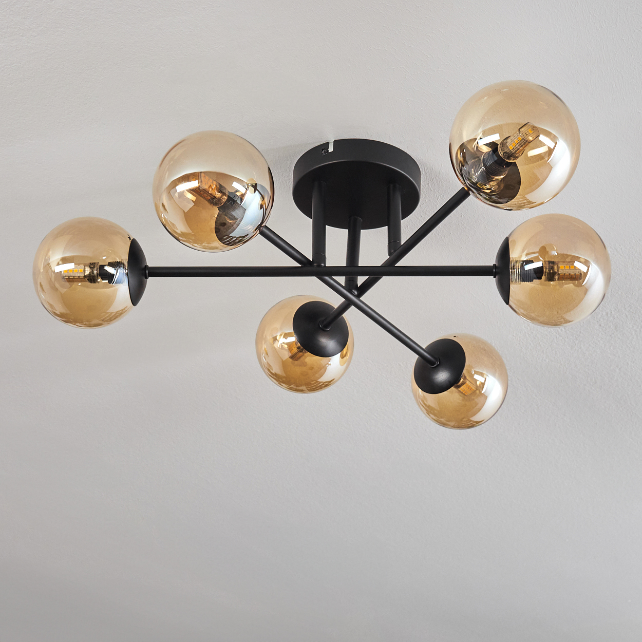 Eine Deckenlampe mit sechs bernsteinfarbenen Glasschirmen. Die Lampe ist an.