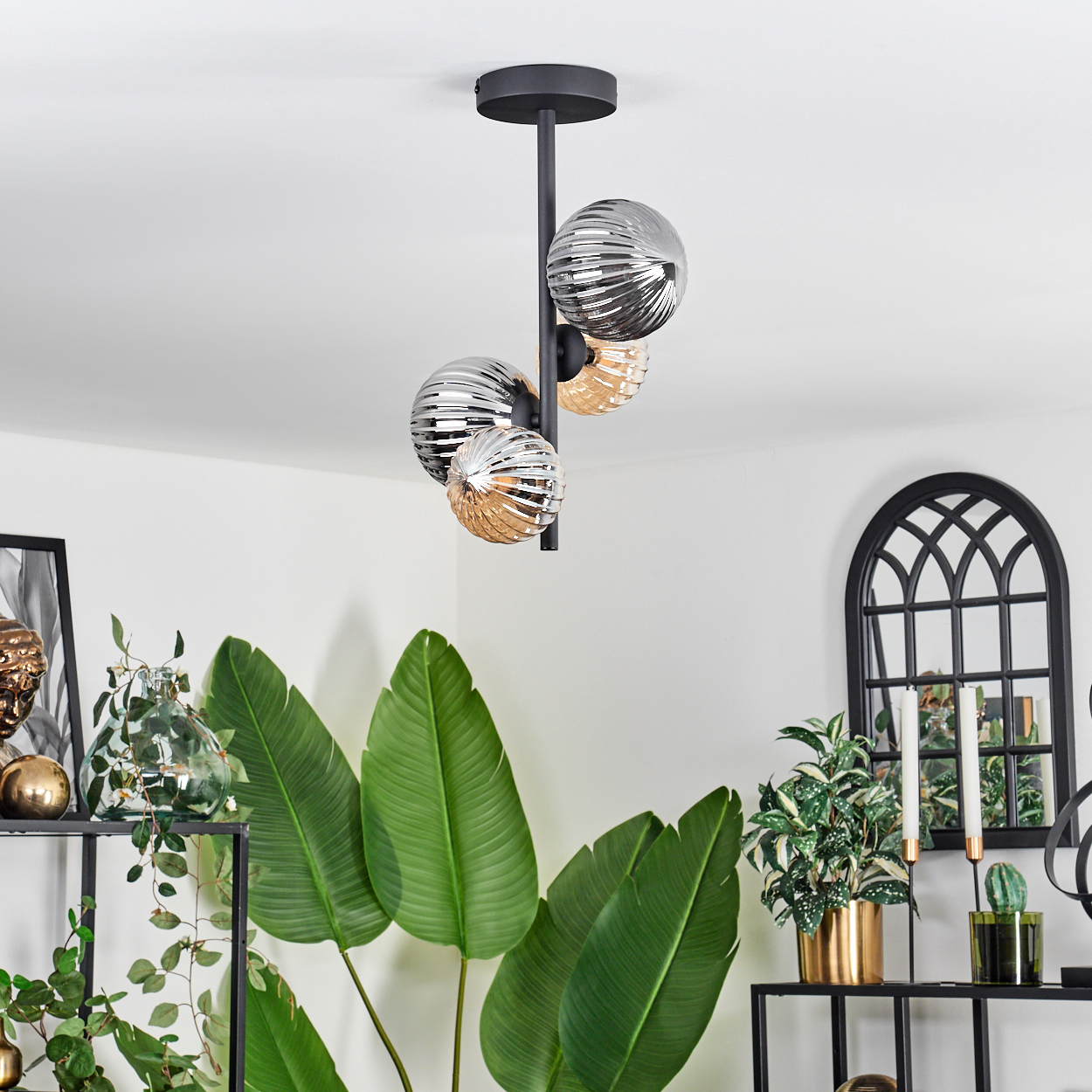 Deckenlampe mit vier Glasglobus, Silber und Gold, in einem Raum mit grünen Pflanzen und einem schwarzen Regal.