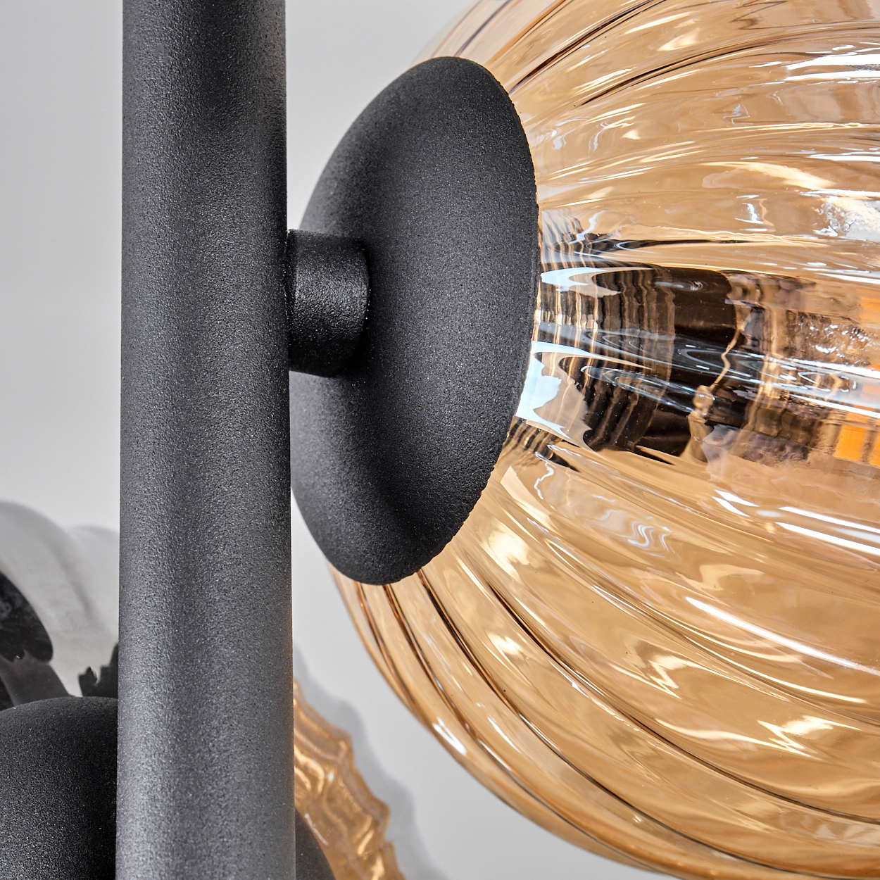 Nahaufnahme einer schwarzen Metallhalterung, die einen geriffelten bernsteinfarbenen Glaskolben hält. Der Globus hat eine warme Glühbirne.