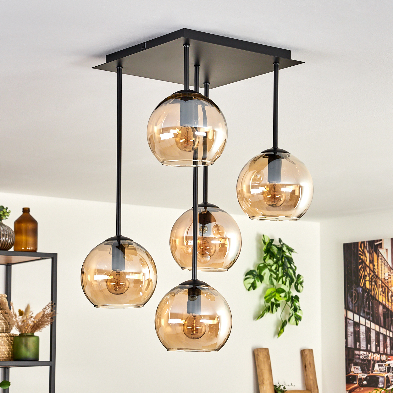 Deckenlampe mit fünf bernsteinfarbenen Glaskugeln. Schwarzer Rahmen. Pflanzen und Deko im Hintergrund.