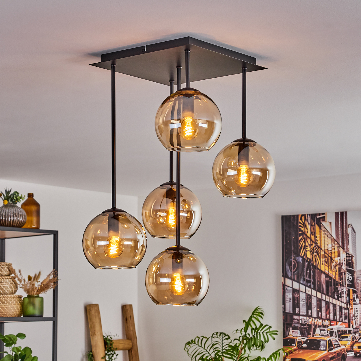 Deckenlampe mit fünf bernsteinfarbenen Glaskugeln. Schwarzer Rahmen. Innenraum mit Pflanzen und Deko.