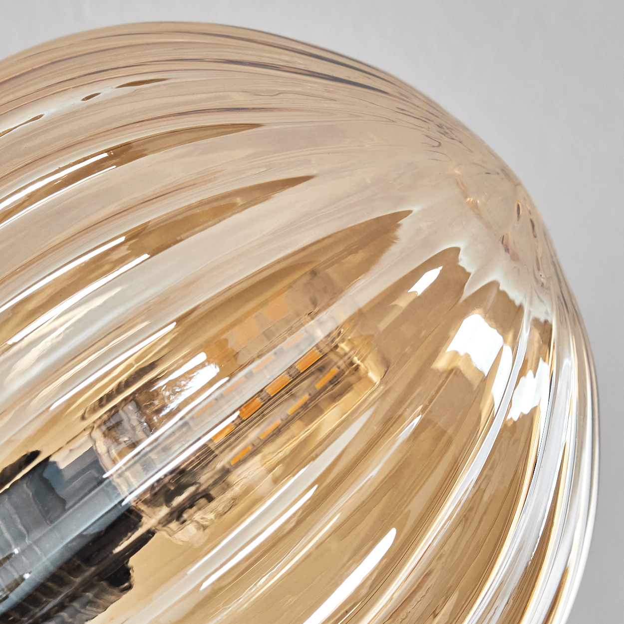 Nahaufnahme einer Glühbirne mit Spiralmuster und bernsteinfarbener Farbe, Licht scheint von innen.