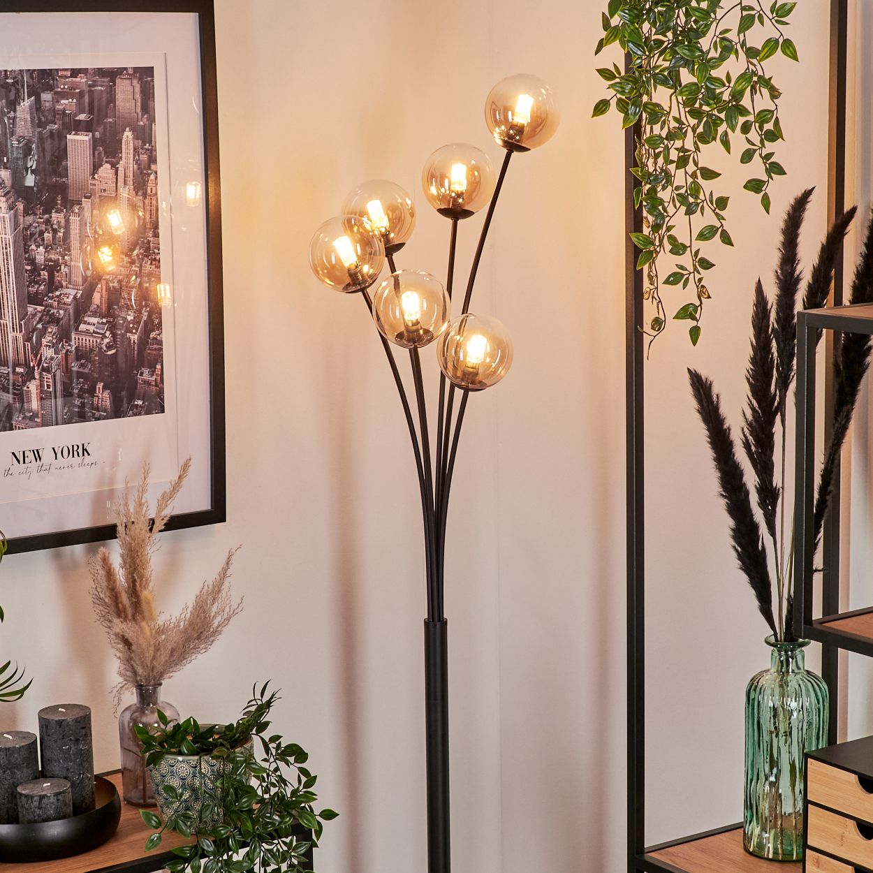 Raumszene mit Stehlampe mit bernsteinfarbenen Kugeln, Bild, Pflanzen und Dekoration auf Regalen.