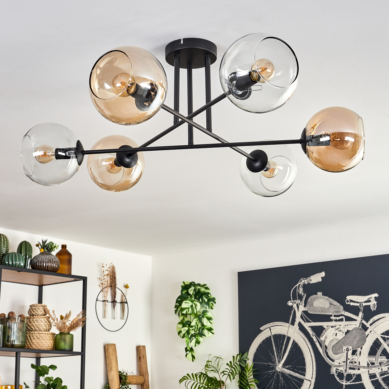 Eine Deckenlampe mit sechs orangefarbenen Glaskugeln, die durch schwarze Metallstäbe verbunden sind. Der Hintergrund ist ein Raum.