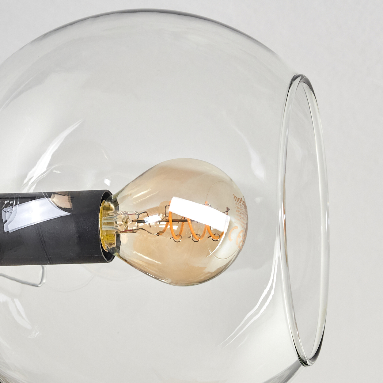 Nahaufnahme einer klaren Glühbirne mit einem Spiralglühfaden in einem orangefarbenen Glasschirm.