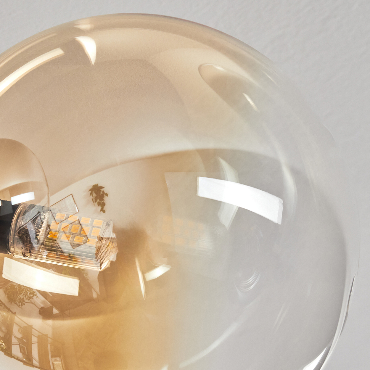 Nahaufnahme einer transparenten, runden Glühbirne mit orangefarbenem Glas. Helles Licht scheint hinein.