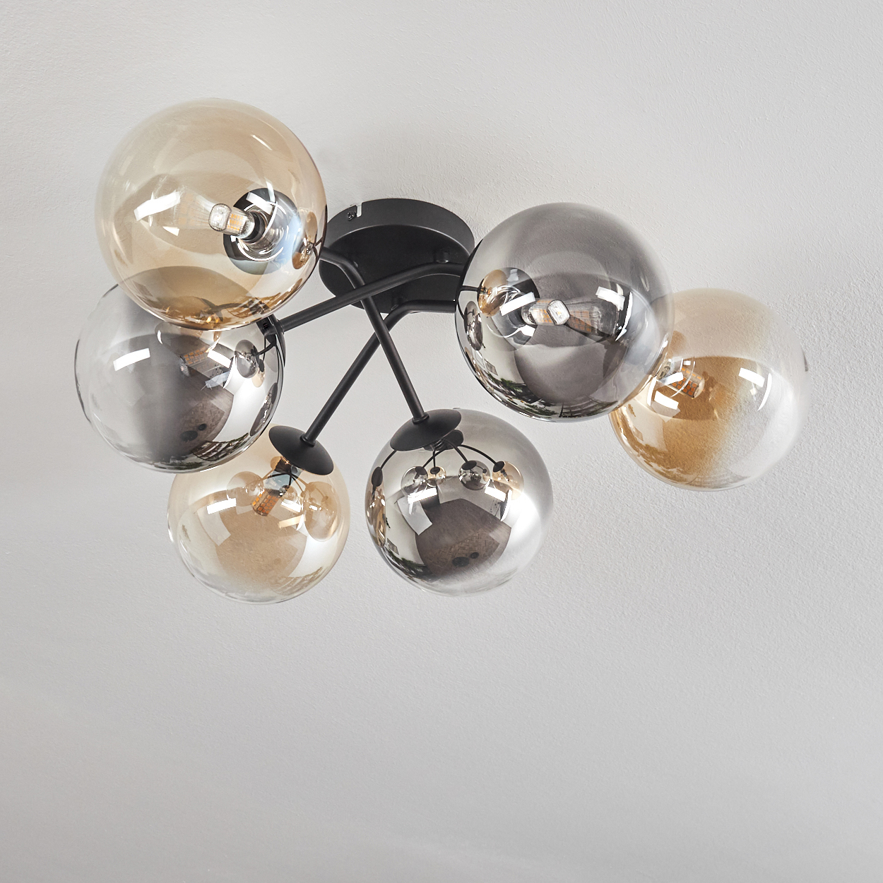 Eine Deckenlampe mit schwarzem Rahmen und mehreren Glaskugelschirmen, vor weißer Decke.