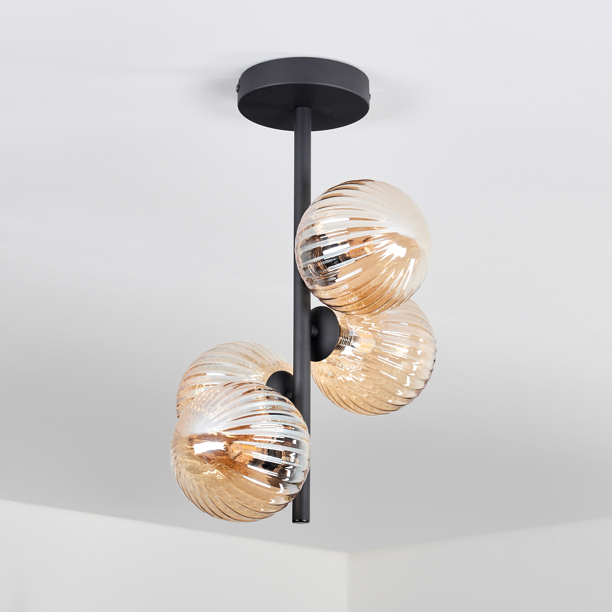Eine schwarze Deckenlampe mit drei bernsteinfarbenen Glaskugelschirmen, vor weißem Hintergrund.